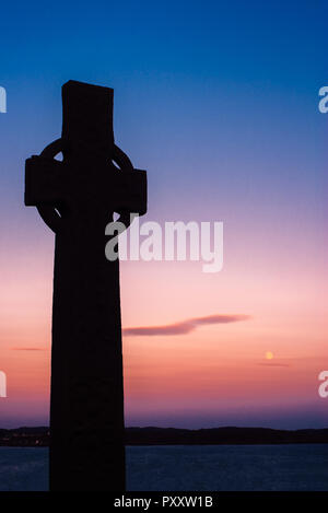 Croce celtica e la luna al tramonto sull'Isola di Iona, Scotland, Regno Unito Foto Stock