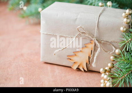 Confezione regalo avvolto in pianura carta marrone, legato con una corda con un legno piccolo albero di natale su un tavolo in legno e un ramo di pino.stile rustico. Selective Foto Stock