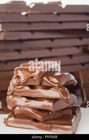 Pila di fusione del cioccolato pezzi con grande pila di cioccolato su sfondo, colpo verticale Foto Stock