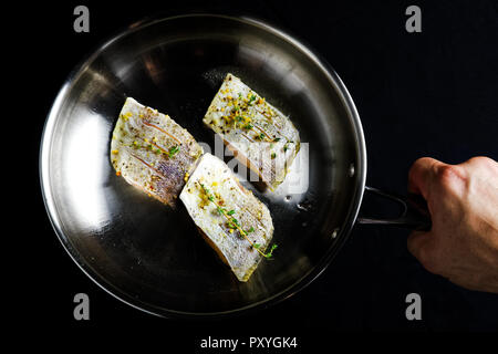 Una mano che tiene tre filetti di pesce con le erbe aromatiche e le spezie in una padella pronto per essere fritto. Foto Stock