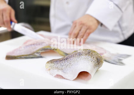 Un grande zander filetto di pesce giacente su un bianco tagliere. Uno chef sfilettatura un pesce in background. Foto Stock