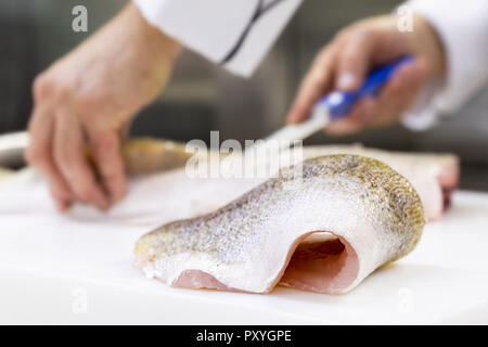 Un grande zander filetto di pesce giacente su un bianco tagliere. Uno chef sfilettatura un pesce in background. Foto Stock