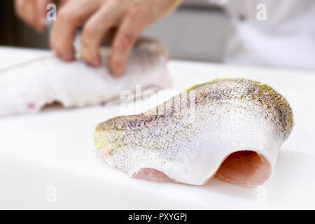 Un grande zander filetto di pesce giacente su un bianco tagliere. Uno chef sfilettatura un pesce in background. Foto Stock