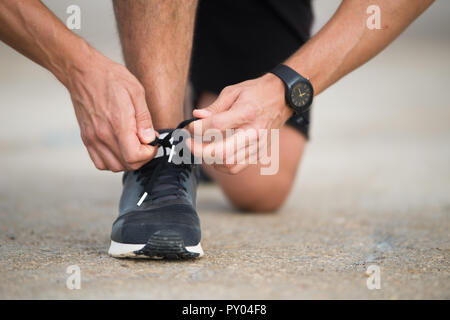 Close-up di sportivo sneakers di legatura. Irriconoscibile uomo arresto scarpa allacciatura all'esterno. Scarpe da ginnastica concetto Foto Stock