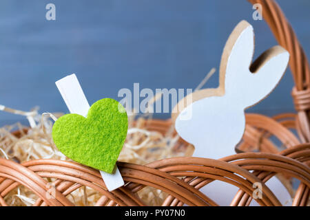 Cuore verde con molla coniglietto di pasqua nel cesto di vimini. In legno naturale dello sfondo. Foto Stock