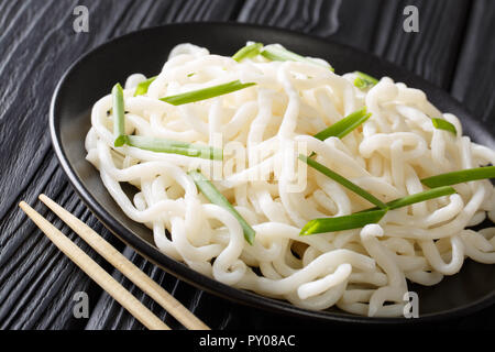 La dieta asiatica di udon tagliatelle con cipolle verdi close-up su una piastra su una tavola nera orizzontale. Foto Stock