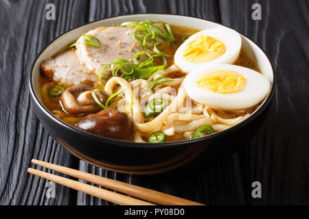 Cucinata fresca zuppa di udon noodles, maiale, uova sode, i funghi e le cipolle verdi close-up in una ciotola su una tavola nera orizzontale. Foto Stock