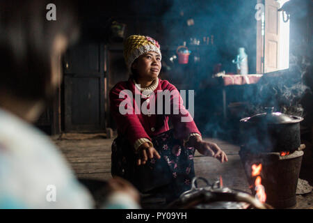 Giovane donna accovacciata di fronte piscina falò e riscaldare le mani, Myanmar, Shan, Myanmar Foto Stock