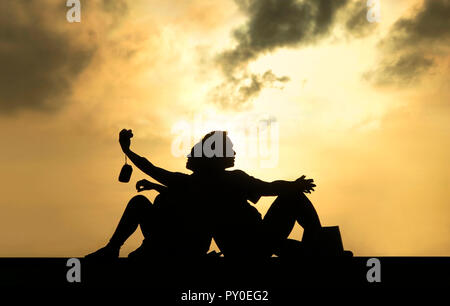 Vista laterale e la silhouette di un giovane seduto di schiena al tramonto e tenendo selfie Foto Stock