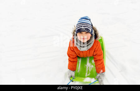 Happy little boy riding sled sulla neve in inverno Foto Stock