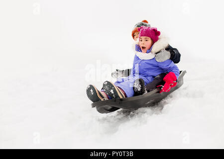 Kids scorrevole sulla slitta verso il basso la collina di neve in inverno Foto Stock