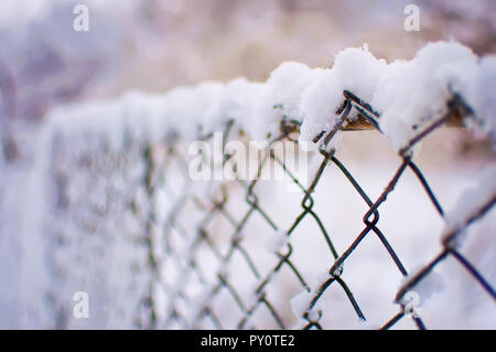 Primo piano di una maglia recinto coperto di uno strato spesso di fresco bianco neve soffice contro una offuscata viola e sfondo arancione. Inverno freddo giorno di gennaio Foto Stock