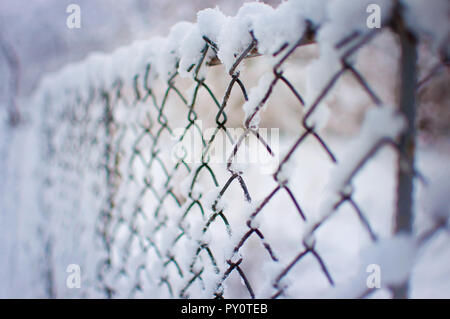 Primo piano di una maglia recinto coperto di uno strato spesso di fresco bianco neve soffice contro a sfocare lo sfondo viola. Inverno freddo giorno di gennaio Foto Stock