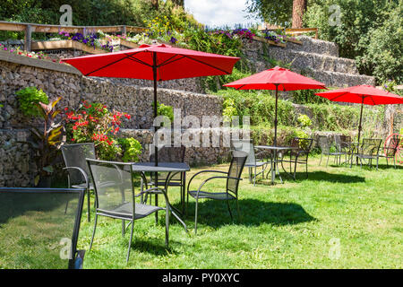 Al di fuori di cafe tavoli sul prato verde sotto le tettoie di rosso Foto Stock