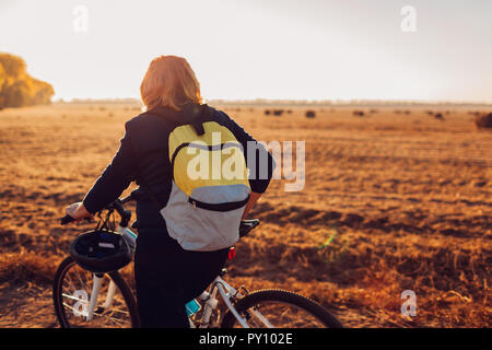 Giovane ciclista di equitazione in campo al tramonto Foto Stock