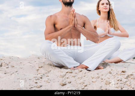 Ritagliato colpo di coppia giovane meditazione seduti sulle dune di sabbia in lotus pongono (padmasana) Foto Stock