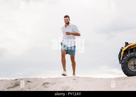 Attraente giovane uomo in esecuzione sulla duna di sabbia nella parte anteriore del cielo molto nuvoloso Foto Stock