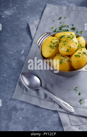 Hot patate bollite in un piatto cosparso di erbe con posate su sfondo grigio Foto Stock