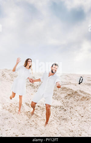 Giocoso coppia giovane tenendo selfie con monopiede e smartphone nel deserto Foto Stock