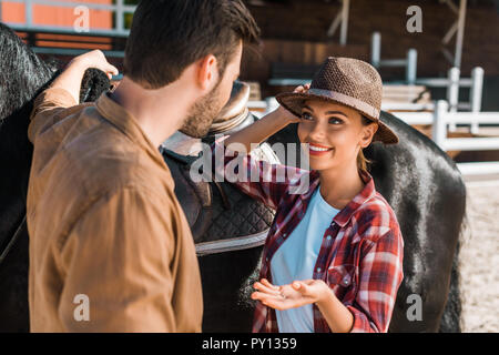 Cowboy e cowgirl in piedi vicino a cavallo e parlando al ranch Foto Stock