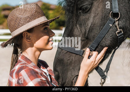 Ritratto di donna attraente toccando equestre e guardando a cavallo al ranch Foto Stock