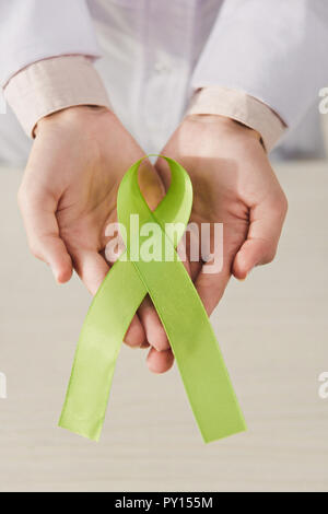 Vista parziale del medico tenendo premuto il nastro verde in mani - si celebra la Giornata mondiale della salute mentale Foto Stock