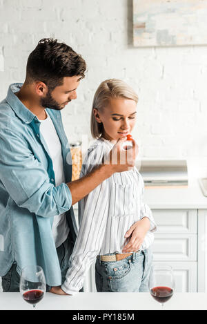 Bel ragazzo ragazza di alimentazione con pomodoro ciliegino in cucina Foto Stock