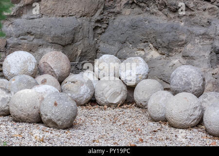 Vecchio palle di cannone di pietra grigia giacente su i ciottoli ai piedi della roccia. Foto Stock