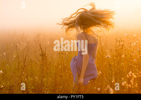 Danza bella ragazza nella nebbia, campo sun retroilluminazione, Sunrise, Orange colori Foto Stock