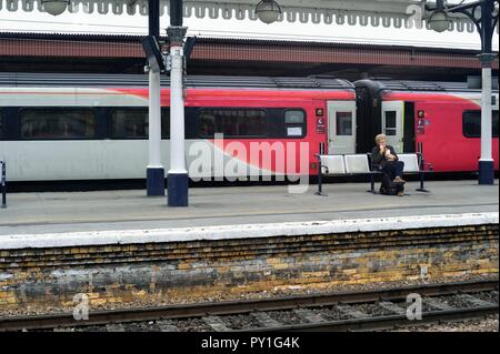 York, Inghilterra, Regno Unito. Un uomo spuntini su un banco di lavoro mentre è in attesa per l arrivo del suo treno su una piattaforma nella stazione di York. In background Foto Stock