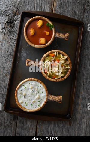 Vista aerea di tre ciotole di zuppa su una placca da forno. Varie zuppe includono, Clam Chowder, pomodoro e pollo noodle. Foto Stock