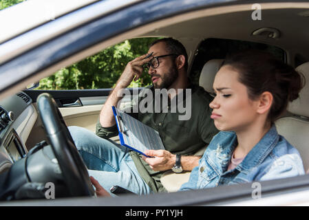 Insoddisfatto maestro toccando la fronte in auto durante la guida di prova Foto Stock