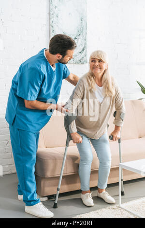 Infermiere sorridente di supporto senior donna con le stampelle Foto Stock
