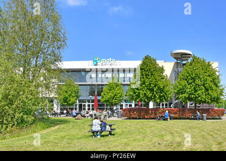 Moto Hospitality M1 motorway services logo & persone break viaggio mangiare all'aperto indietro di un ristorante fast food erba & tavoli da picnic LEICESTERSHIRE REGNO UNITO Foto Stock