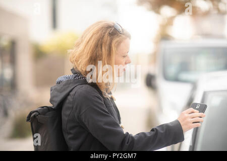 Donna in piedi da una vettura aprendo la porta con il suo telefono cellulare Foto Stock