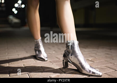 Ritagliato colpo di donna in argento lucido stivali camminando sulla strada di notte Foto Stock