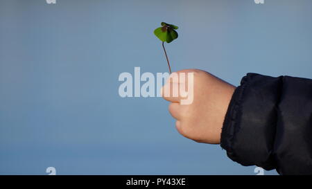 Bambino la mano che regge un quattro Leaf Clover contro un cielo blu Foto Stock