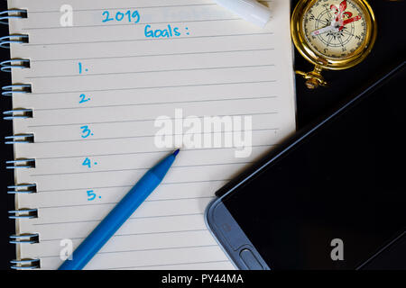 Notebook, Smartphone, bussola e penna, con fuoco selettivo 2019 testo obiettivi in mano di qualcuno con sfondo nero, per presentazioni aziendali ror addin Foto Stock