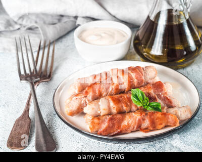 Pronti da consumare insaccati suini avvolto in pancetta sulla piastra. Fritti gustosi insaccati avvolto in pancetta servito fresco verde foglie di basilico con salsa di sfondo. DOF poco profondo. Copia spazio per il testo. Foto Stock