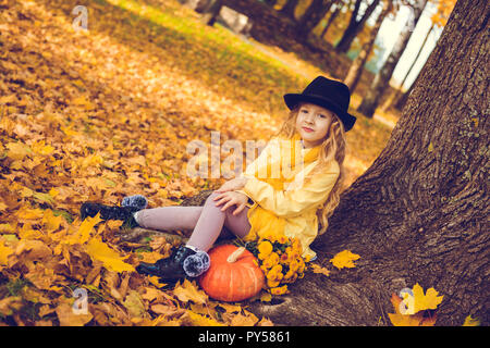 Poco bella ragazza bionda con grande zucca in autunno sfondo Foto Stock