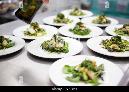 Collegamenti alimentare 2015. Uno chef stride Olio Extra Vergine di Oliva su un piatto vegetariano in una cucina commerciale. Foto Stock