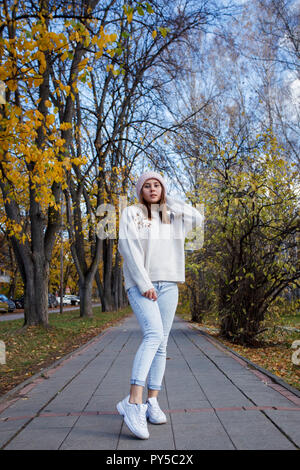 Tanga elegante ragazza in bianco beanie, blue jeans e maglia giacca. All'aperto, lifestyle, autunno autunno camminare per strada Foto Stock