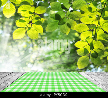 Tabella vuota con verde tovaglia gingham oltre fresche foglie verde dello sfondo. Ottimo per la visualizzazione del prodotto montaggi Foto Stock