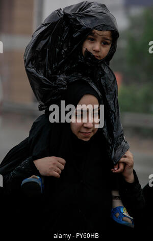 Baghdad in Iraq. 25 ott 2018. Sciita irachena pellegrino porta in sé il figlio come ella rende il loro modo per la tomba di Imam Hussain durante un giorno di pioggia per eseguire la cerimonia religiosa il quarantesimo giorno dopo la santa sciita giorno di Ashura che commemora la morte di imam Hussein nella battaglia di Karbala. Credito: Ameer Al Mohammedaw/dpa/Alamy Live News Foto Stock