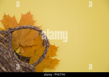 Foglie di autunno e un cesto su uno sfondo giallo, il concetto di autunno. Foto Stock
