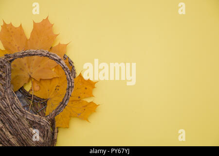 Foglie di autunno e un cesto su uno sfondo giallo, il concetto di autunno. Foto Stock