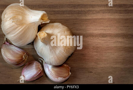 Vista dall'alto di due teste di aglio e sciolto spicchi di aglio su una superficie di legno con spazio per il testo. Foto Stock