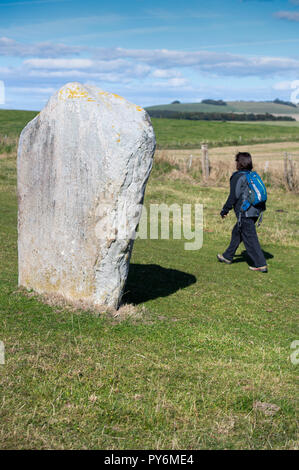 Donna passato a piedi una delle pietre che compongono l'Avebury Stone cerchi in Inghilterra, Regno Unito