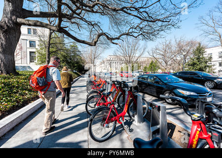 Washington DC, Stati Uniti d'America - Aprile 5, 2018: capitale bikeshare rosso Riga biciclette sul marciapiede street nella città capitale, giovane gente che cammina, ampio angolo, su strada Foto Stock