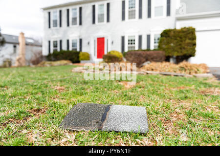 Cortile anteriore di casa durante il giorno dopo dopo la tempesta tegola di tetto di scandole sdraiati sull'erba, danni closeup Foto Stock